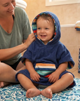 Woman helping a child in a blue hooded towel in a bathroom.