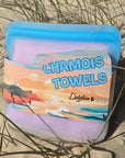 2 pack chamois cloth, in a silicone storage case being displayed on the beach.