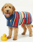 Dog wearing a colorful striped dog drying coat and anxiety coat, with a yellow rubber duck on a white background, The coat is a wearable dog towel and bathrobe