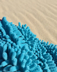 Close-up of a blue dog towel with a sand background, dog towel has noodle type fingers and is made of microfibre