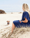 women's hooded towel being worn on the beach, hooded towel is reversible. navy blue one side and striped on the other