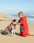 dog and a kid wearing matching hooded towels on the beach.