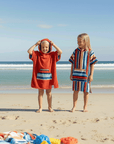 Two children on a beach wearing colorful surf ponchos with ocean and sky in the background