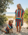 Woman and her dog at the beach wearing matching towels, dog is wearing a striped dog robe and the women a striped hooded towel