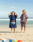 Two children on a beach wearing colorful kids hooded towels, with ocean and sky in the background