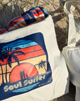 A tote bag with an artist print of a women surfer and a dog, text on tote bag says 'Soul Surfer' by Dolphin & Dog.
