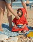 a toddler wearing a hooded towel at the beach with his mum