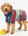 A wet dog wearing a colorful wearable dog towel with a rubber duck on a white background.