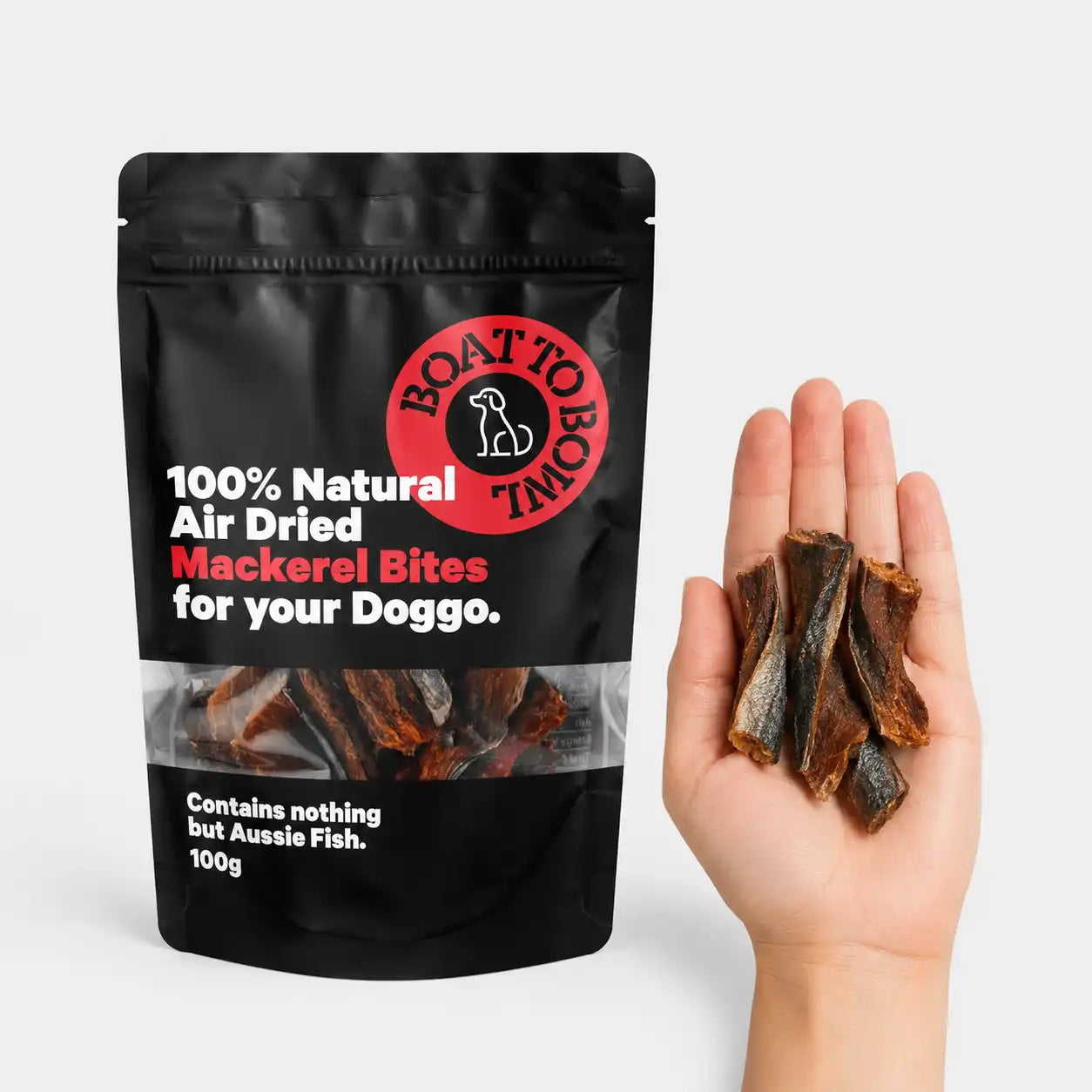 Air-dried mackerel dog treats shown in a hand beside a 100g mackerel bites pouch for size comparison.