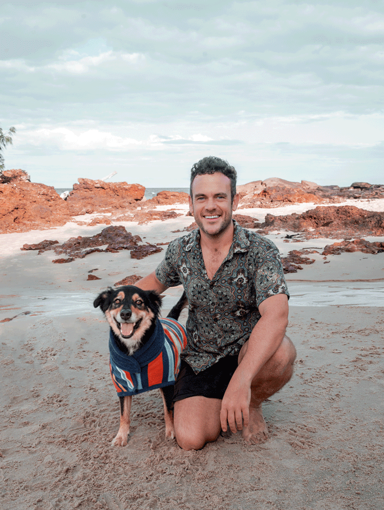 dog wearing a dog robe, along side a man at the beach