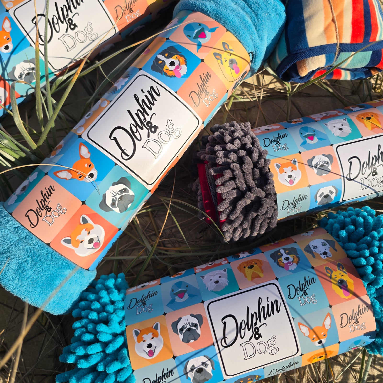 The Dolphin and Dog Towel range displayed on the beach. premium dog towels in their bright packaging 
