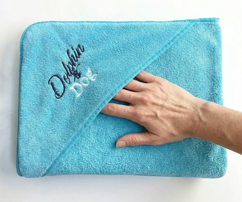 Blue towel with 'Dolphin & Dog' embroidery on a white background showing the hand pocket.