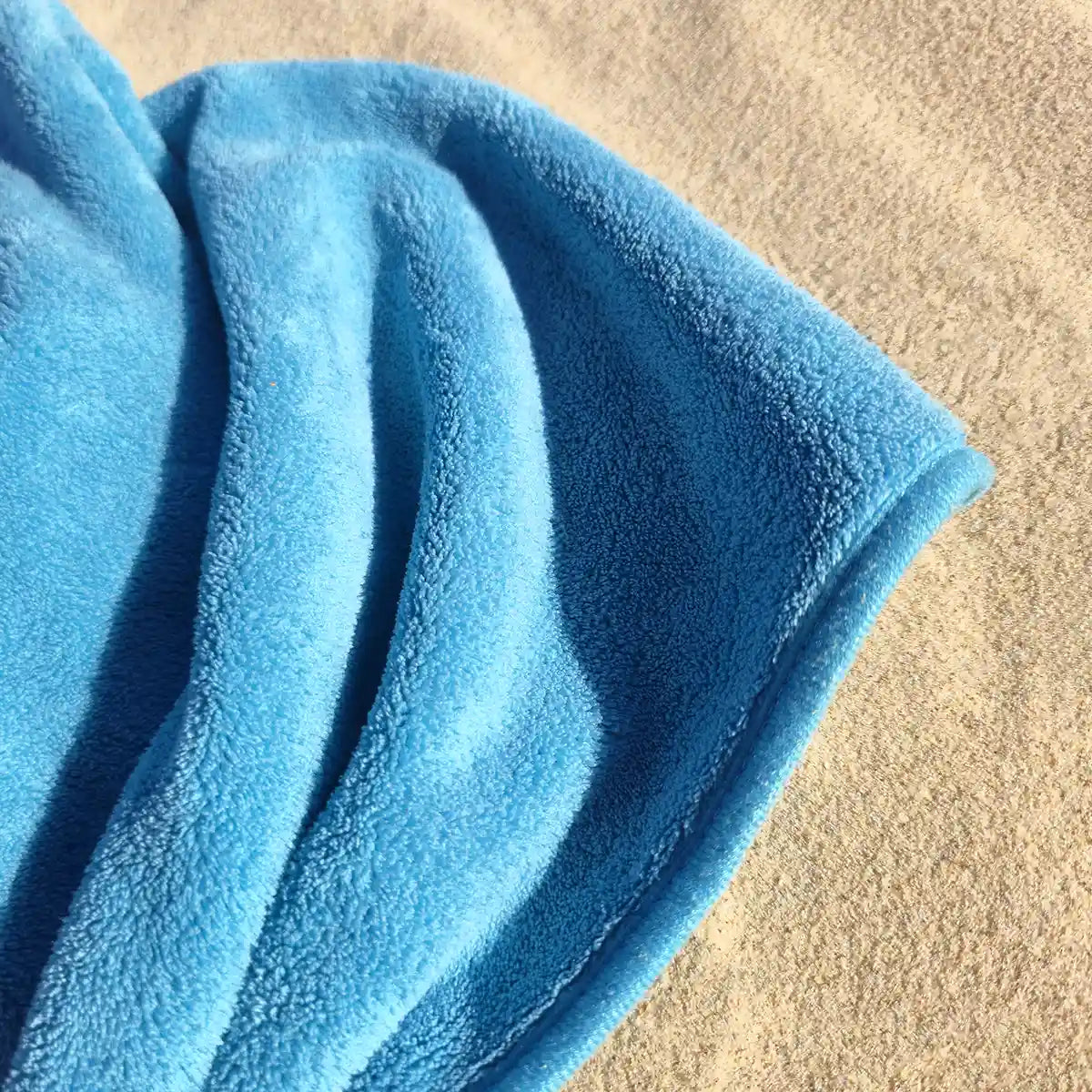 a blue dog towel laying on the sand at the beach, towel has a very soft looking texture.
