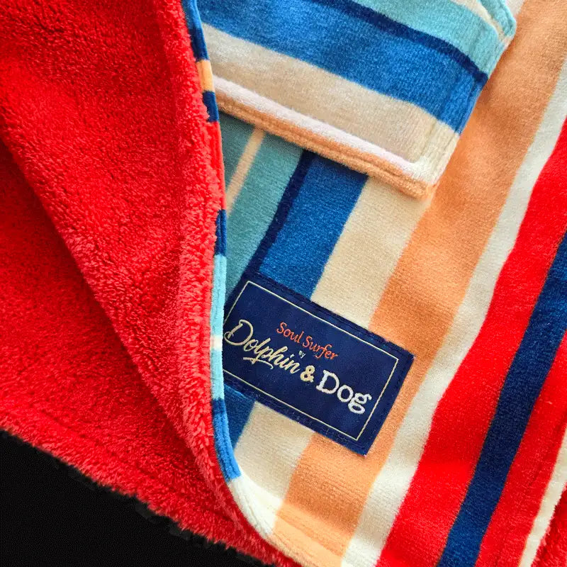 Close-up of a hooded towel with a brand label 'Dolphin &amp; Dog', featuring red, blue, and orange stripes.