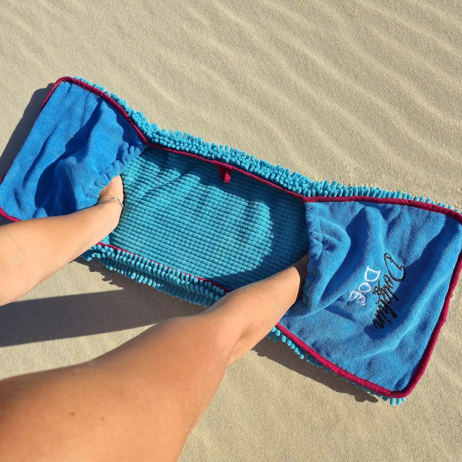 Dolphin & Dog fast drying dog towel held open on the beach, showing hands in the corner pockets for easy drying.