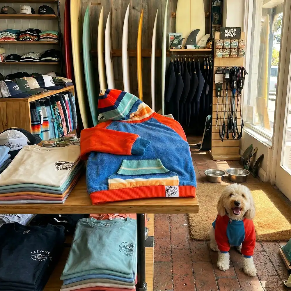 a dog hoodie on display in a surf ship, the dog hoodie is brightly coloured and shows a pockets and hood design, 