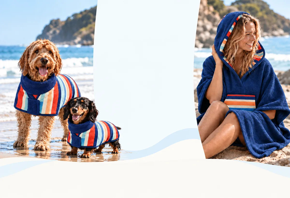 Dogs wearing Dolphin & Dog drying robes beside a woman wearing a matching hooded beach towel.