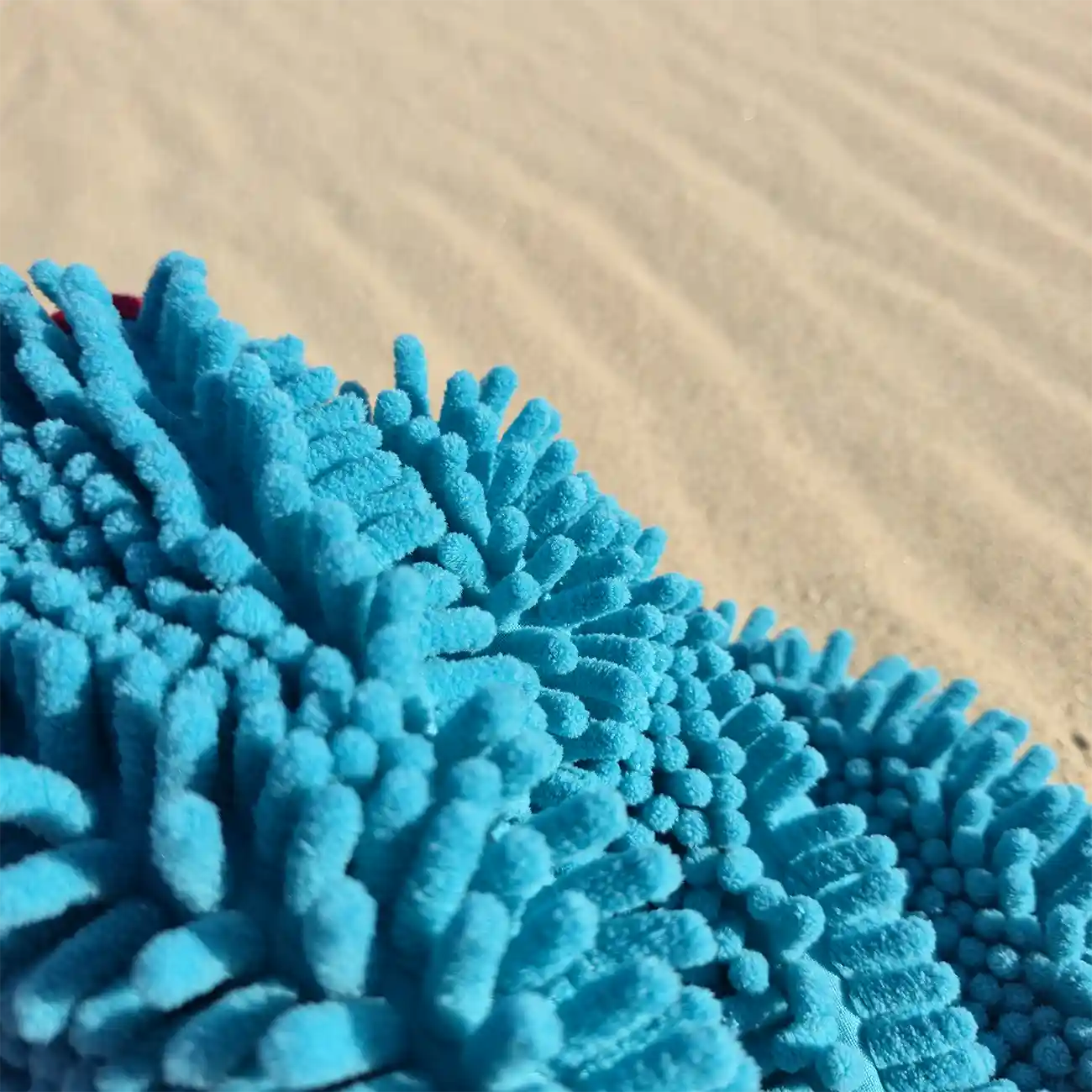 Close-up of a blue dog towel with a sand background, dog towel has noodle type fingers and is made of microfibre 