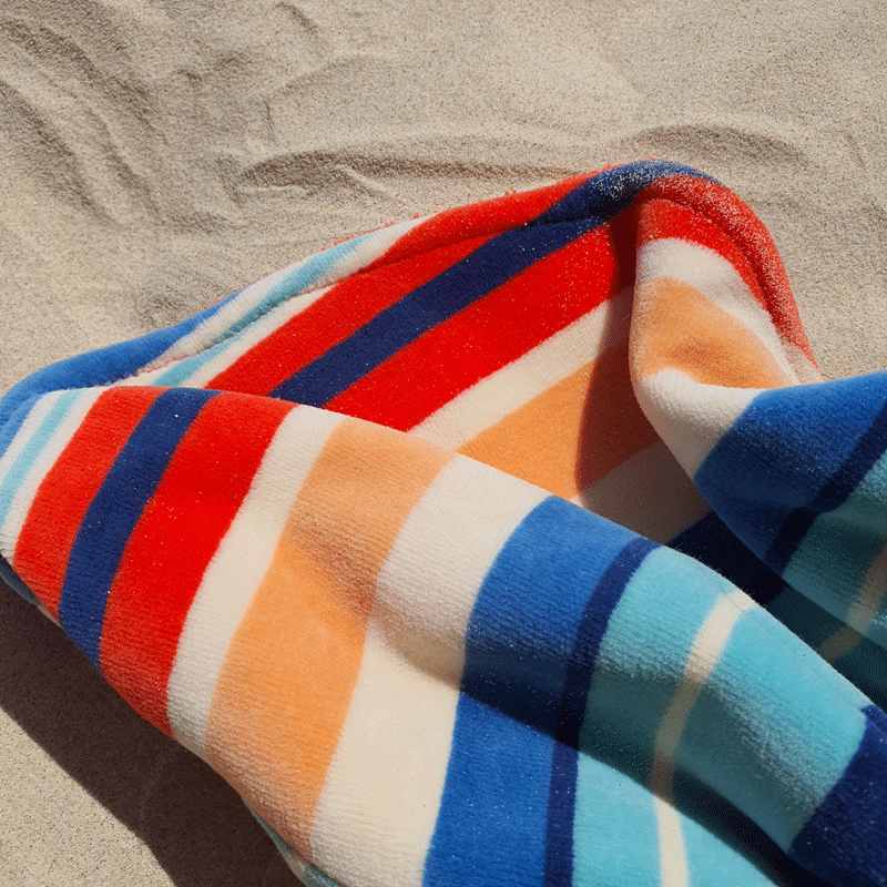 a close up of the Dolphin and Dog towel, on the sand at the beach