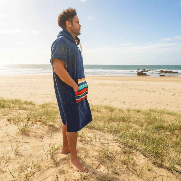 Man standing on a beach wearing a blue hooded towel with a colorful striped pattern.