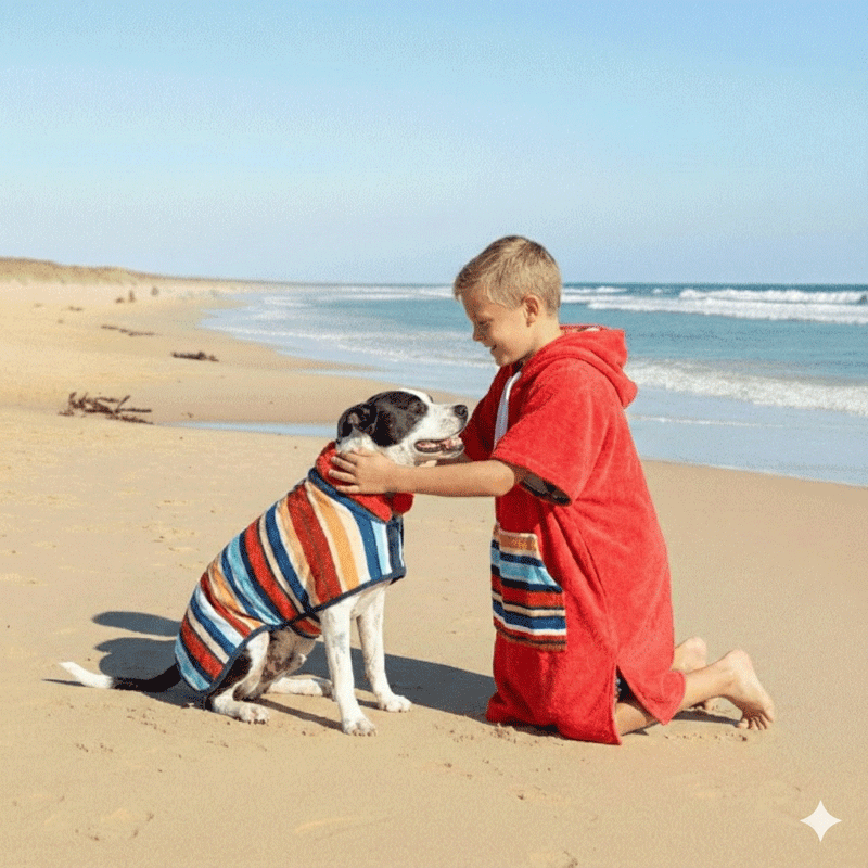 dog and a kid wearing matching hooded towels on the beach.