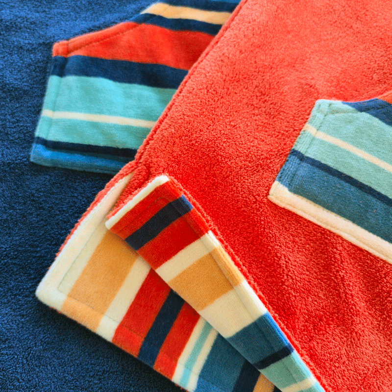 A kids and a baby hooded striped towel and a red towel on a blue background
