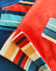 A kids and a baby hooded striped towel and a red towel on a blue background