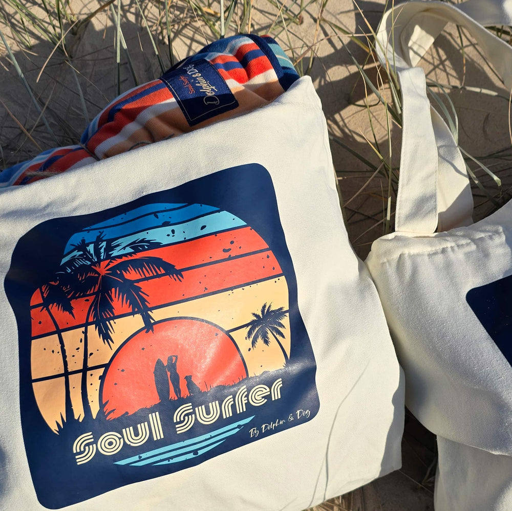 A tote bag with an artist print of a women surfer and a dog, text on tote bag says 'Soul Surfer' by Dolphin & Dog. 