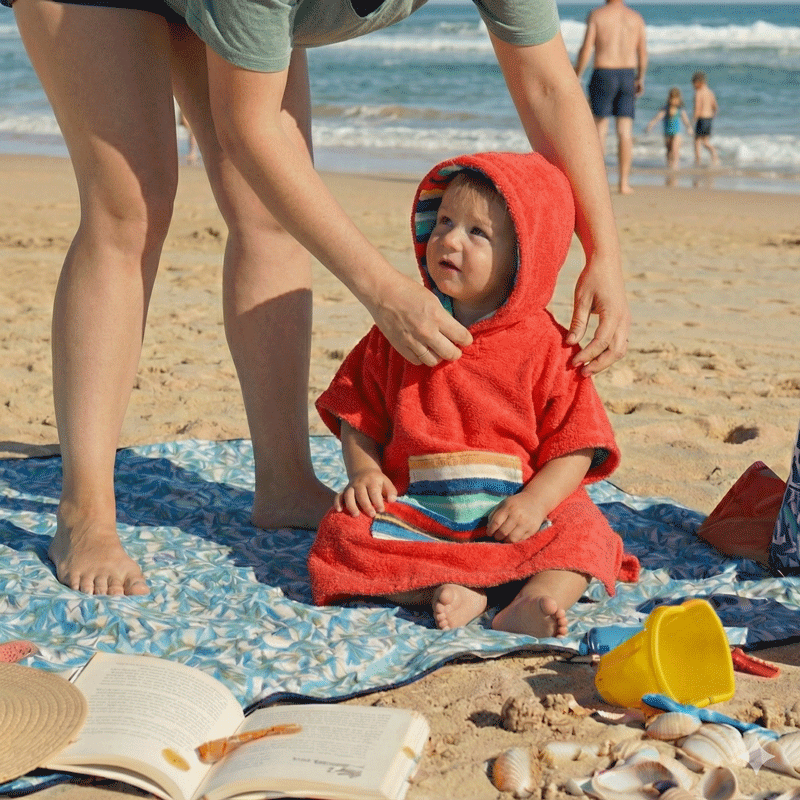 a toddler wearing a hooded towel at the beach with his mum