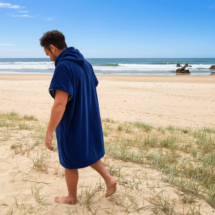 Person walking on a beach wearing a blue hooded towel.