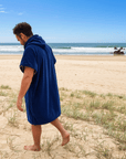 Person walking on a beach wearing a blue hooded towel.